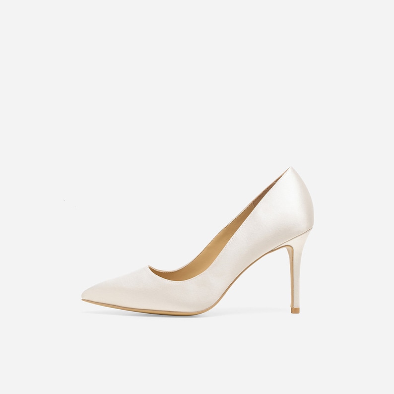 May include: A pair of ivory satin pumps with a pointed toe and a stiletto heel.