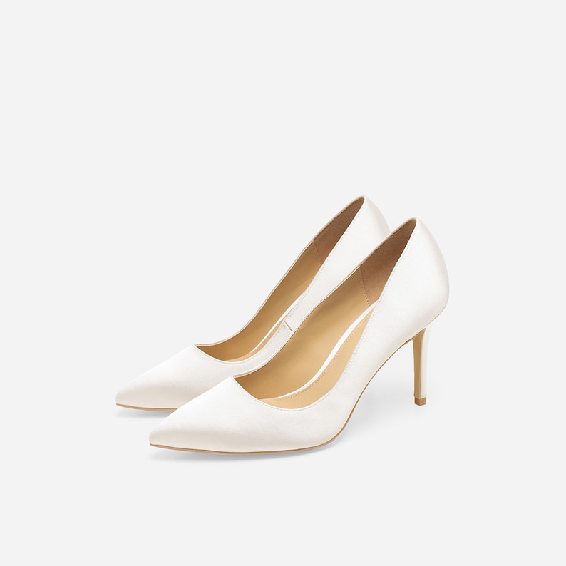 May include: A pair of white satin pumps with a pointed toe and stiletto heels.