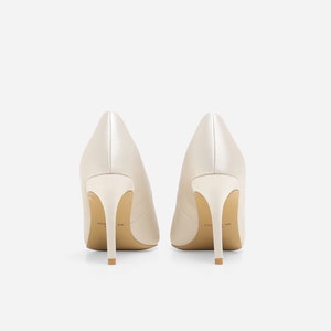 May include: A pair of ivory satin high-heeled pumps with a pointed toe. The heels are about 3 inches tall and the shoes have a subtle sheen.