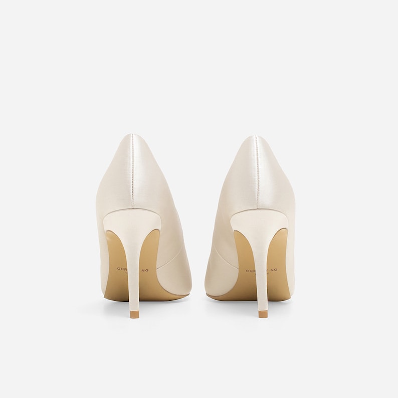 May include: A pair of ivory satin high-heeled pumps with a pointed toe. The heels are about 3 inches tall and the shoes have a subtle sheen.