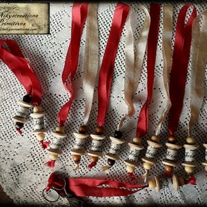 Puede incluir: Diez carretes de madera con la palabra "Scissor" escrita en ellos están ensartados juntos con una cinta roja y crema. Los carretes están decorados con cuentas marrones y blancas. Los carretes están colgados de un mantel de encaje blanco.