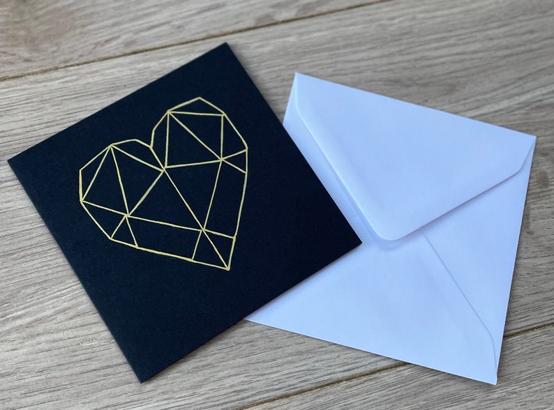 May include: A black card with a gold geometric heart design. The card comes with a white envelope.