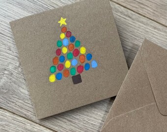 May include: A square, brown Christmas card with a hand-painted Christmas tree design. The tree is made of colorful dots in red, blue, yellow, and orange, topped with a yellow star. A matching brown envelope is next to the card.