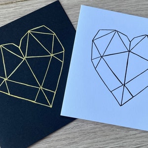 May include: Two cards with geometric heart designs. One card is black with a gold heart, the other is white with a black heart.