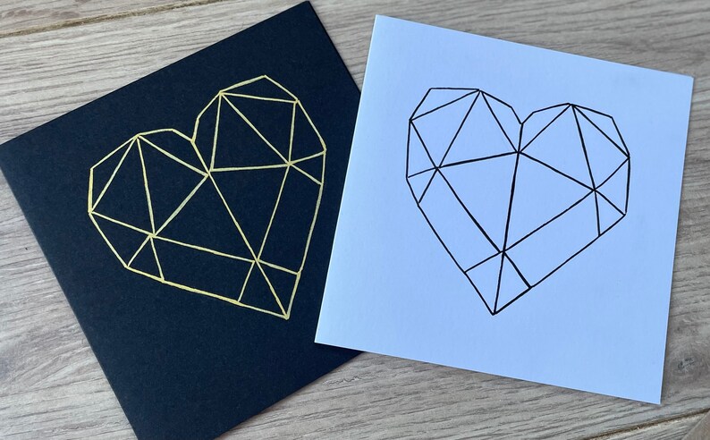 May include: Two cards with geometric heart designs. One card is black with a gold heart, the other is white with a black heart.
