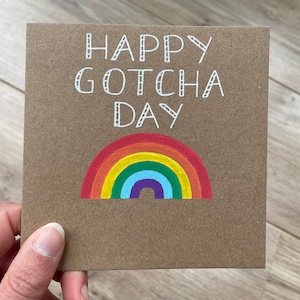 May include: A brown card with the text "Happy Gotcha Day" written in white. A rainbow is drawn below the text.