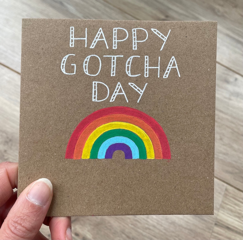 May include: A brown card with the text "Happy Gotcha Day" written in white. A rainbow is drawn below the text.