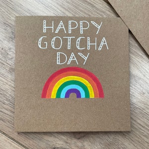 May include: A brown card with the text "Happy Gotcha Day" in white lettering. A rainbow is drawn below the text.