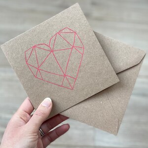 May include: A brown card with a pink geometric heart design. The card is folded in half and has a brown envelope.