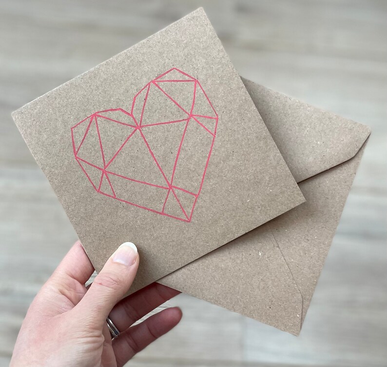 May include: A brown card with a pink geometric heart design. The card is folded in half and has a brown envelope.