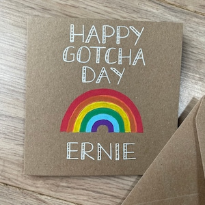 May include: A brown card with the text "Happy Gotcha Day Ernie" in white. A rainbow is drawn below the text.