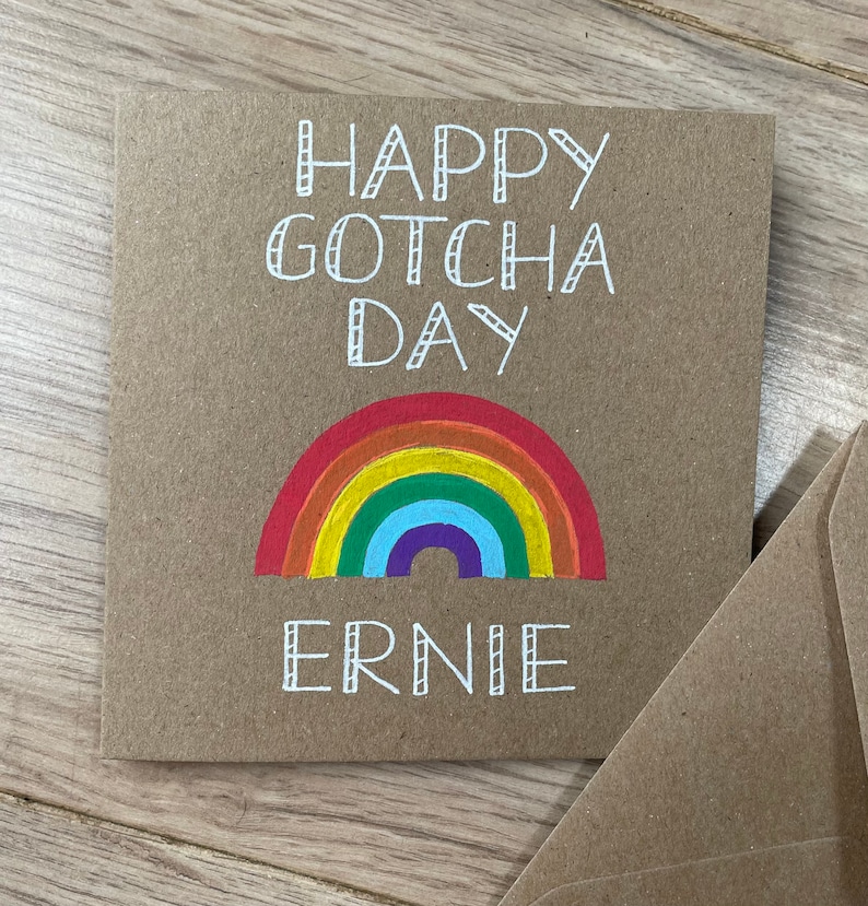 May include: A brown card with the text "Happy Gotcha Day Ernie" in white. A rainbow is drawn below the text.