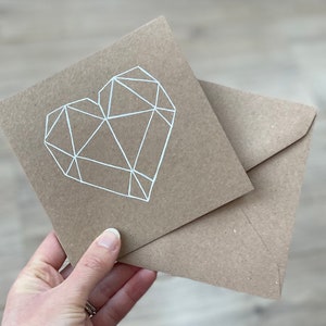 May include: A brown card with a white geometric heart design. The card is folded in half and has a matching brown envelope.