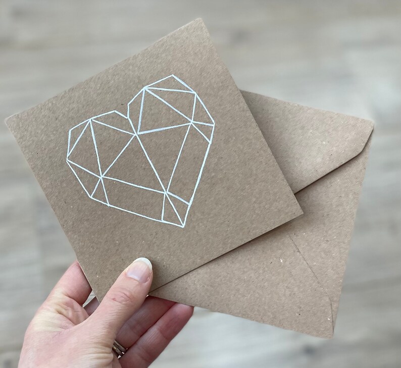 May include: A brown card with a white geometric heart design. The card is folded in half and has a matching brown envelope.