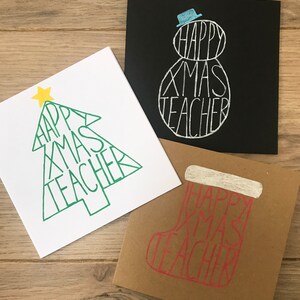 May include: Three Christmas cards with the text "HAPPY XMAS TEACHER". One card is white with a green Christmas tree design, another is black with a snowman, and the third is brown with a stocking.