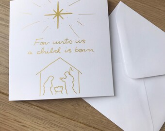 May include: A white Christmas card with gold foil accents. The card features a star, the text "For unto us a child is born," and a nativity scene illustration. A white envelope is included.