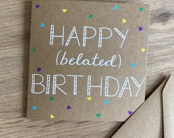 Puede incluir: Una tarjeta marrón con un mensaje escrito a mano en blanco que dice "Feliz cumpleaños (atrasado)". La tarjeta está decorada con confeti de colores.