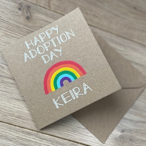 May include: A brown card with the text "Happy Adoption Day" and a rainbow with the name "Keira" written below it.