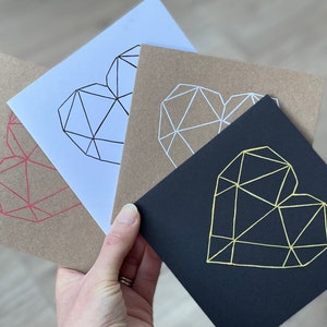 May include: Three greeting cards with geometric heart designs. The cards are brown, white, and black. The hearts are outlined in red, white, and gold.
