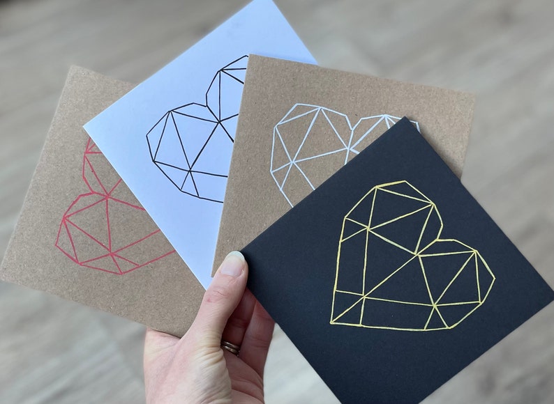 May include: Three greeting cards with geometric heart designs. The cards are brown, white, and black. The hearts are outlined in red, white, and gold.