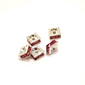 May include: Five silver-toned square-shaped bead caps with a hole in the center. Each bead cap is decorated with pink rhinestones.