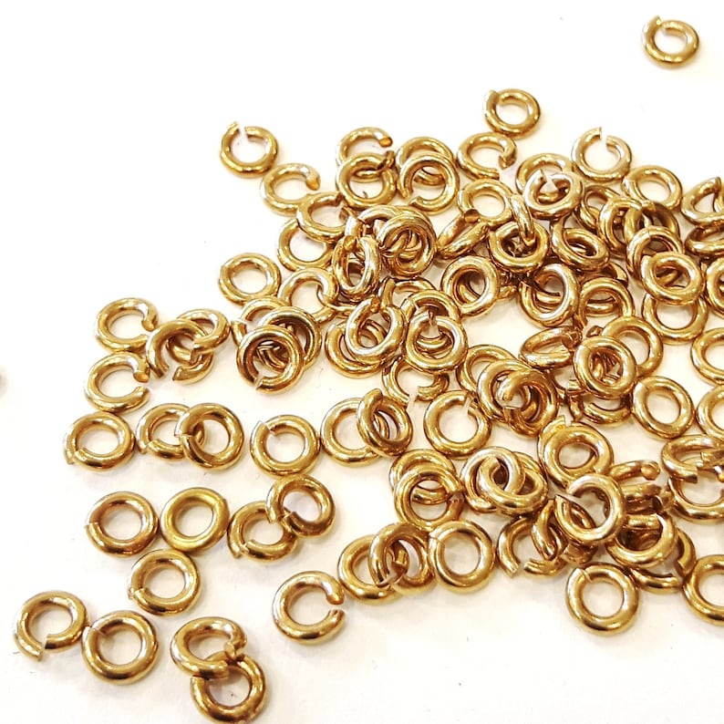 May include: A large pile of gold jump rings, a type of jewelry finding, on a white background.