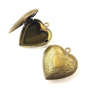 Peut inclure: Deux médaillons antiques en forme de cœur en bronze. L'un est ouvert, révélant l'intérieur. L'autre est fermé, avec un motif de cœur au centre et des motifs floraux sur les bords.