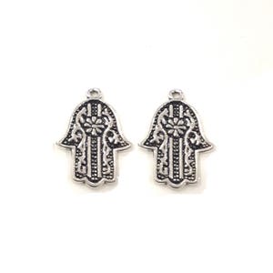 Può includere: Due ciondoli in metallo color argento a forma di mano di hamsa con intricati disegni floreali.