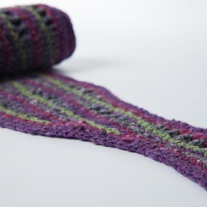 May include: A purple, green, and pink crocheted scarf with a lacy pattern.