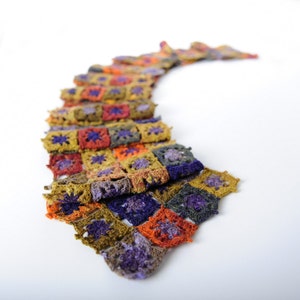 May include: A colorful crocheted scarf with a patchwork design featuring squares in shades of green, orange, purple, and brown.