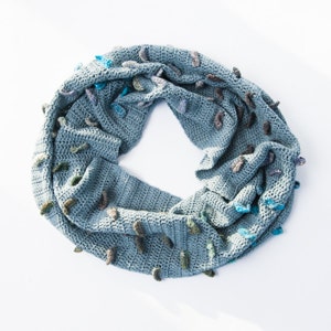 Może przedstawiać: Niebieski, szydełkowy szal w kształcie ósemki z kolorowymi akcentami z włóczki. Szal wykonany jest z fakturowanym ściegiem i ma miękki, przytulny charakter.