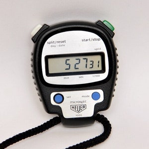 Puede incluir: Un cronómetro negro con una pantalla digital que muestra 52731. El cronómetro tiene una correa negra y botones azules etiquetados como "set" y "mode". La pantalla también muestra "split/reset", "day-date", "start/stop", "split", "min", "sec", "1/100" y "microsplit". El cronómetro está hecho por Heuer.