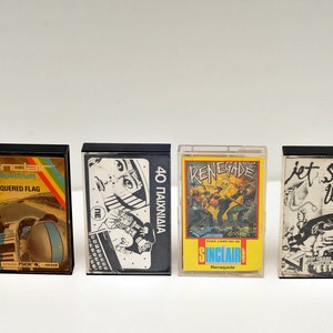 Può includere: Quattro cassette vintage nere con etichette colorate. Le etichette presentano titoli come "Chequered Flag", "Renegade" e "Jet Set Willy".