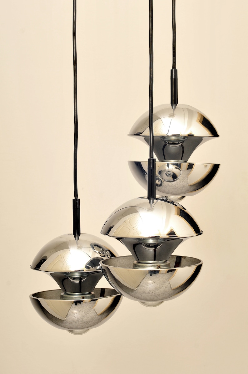 Peut inclure: Un ensemble de trois lampes suspendues en chrome au design unique. Chaque lampe est compos&eacute;e de deux demi-sph&egrave;res superpos&eacute;es, cr&eacute;ant un effet de superposition.