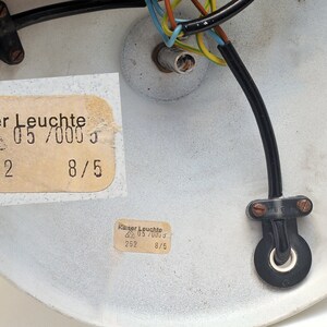 Peut inclure: Gros plan de l'arri&egrave;re d'un luminaire de plafond blanc avec un c&acirc;blage noir et une &eacute;tiquette indiquant "Kaiser Leuchte 05/0003 262 8/5".