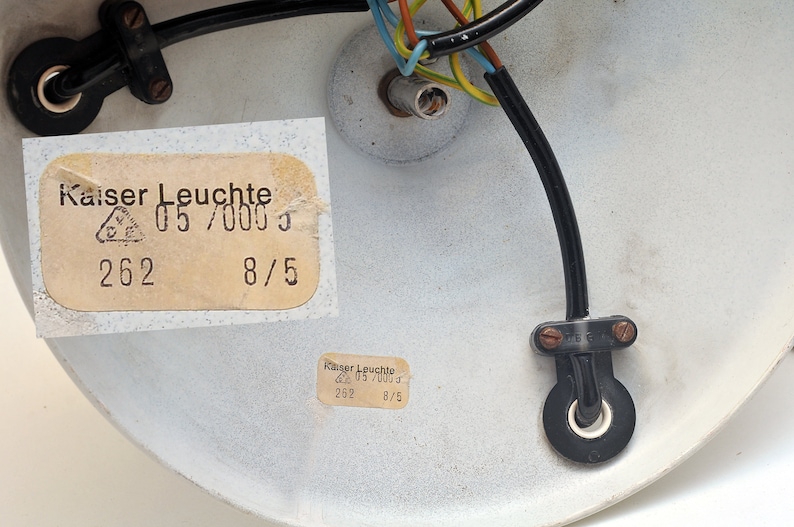 Peut inclure: Gros plan de l'arri&egrave;re d'un luminaire de plafond blanc avec un c&acirc;blage noir et une &eacute;tiquette indiquant "Kaiser Leuchte 05/0003 262 8/5".