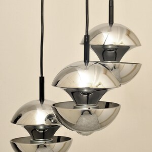 Peut inclure: Trois lampes suspendues chrom&eacute;es avec des cordons noirs suspendus au plafond. Les lumi&egrave;res sont empil&eacute;es les unes sur les autres, la lumi&egrave;re du haut &eacute;tant la plus grande et la lumi&egrave;re du bas &eacute;tant la plus petite.