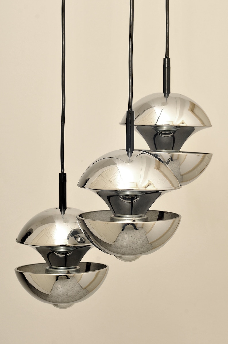 Peut inclure: Trois lampes suspendues chrom&eacute;es avec des cordons noirs suspendus au plafond. Les lumi&egrave;res sont empil&eacute;es les unes sur les autres, la lumi&egrave;re du haut &eacute;tant la plus grande et la lumi&egrave;re du bas &eacute;tant la plus petite.