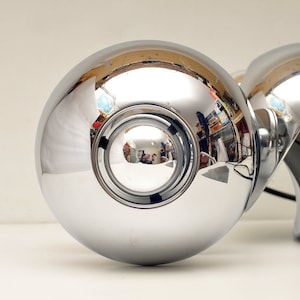 Peut inclure: Un ensemble de trois luminaires de plafond sph&eacute;riques chrom&eacute;s avec une surface r&eacute;fl&eacute;chissante. Les luminaires sont reli&eacute;s par un fil noir.