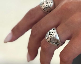 May include: A silver-toned cuff bracelet and two matching silver-toned rings, each featuring an intricate, embossed floral scrollwork pattern. The jewelry pieces have a polished finish and a consistent, detailed engraved design across all items.