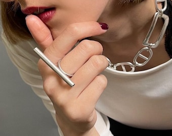 May include: A silver-toned ring featuring a horizontal bar design, a chunky chain-link necklace with elongated oval links, and two smooth silver-toned ear cuffs worn on the upper ear cartilage. The jewelry pieces have a polished metallic finish.