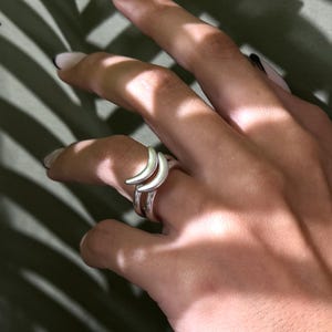 Può includere: Una tazza di ceramica bianca con manico nero e la scritta "But First, Coffee" in nero, con un carattere a mano. La tazza è su una superficie bianca.