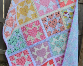 Puede incluir: Una colcha de retazos con un esquema de color rosa, blanco y verde. La colcha está hecha de varios cuadrados con diferentes patrones, incluyendo estrellas, corazones y formas geométricas.