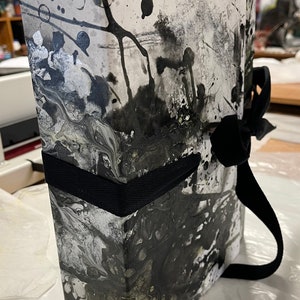 May include: A black and white marbled book with a black ribbon tied around it.