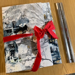 Peut inclure: Un livre d'art abstrait blanc et noir avec un ruban de velours rouge noué autour en forme de nœud. Le livre est sur une surface en bois.