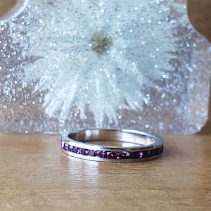 May include: A silver band ring with a row of small, dark purple gemstones.