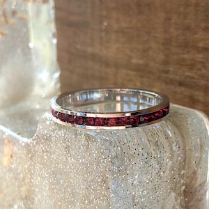 May include: A silver band ring with a row of small, dark red gemstones.