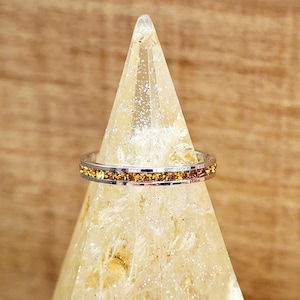 May include: A silver ring with a thin band of orange cubic zirconia stones.