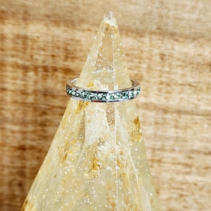 May include: A silver ring with a row of light green cubic zirconia stones.