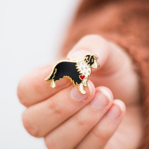 Border collie gold plated hard enamel pin badge. Black and white border collie design with a little red love heart on its chest held in a female hand.